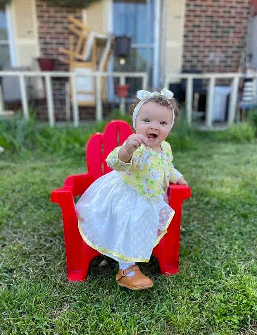 Sage is registered to the contest to win money with this photo: baby, baby_toddler_clothing, bridal_party_dress, chair, child, dress, event, formal_wear, fun, garden, grass, happy, lawn, people_in_nature, person, plant, recreation, sitting, smile, toddler