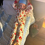Christian is registered to the contest to win money with this photo: child, pajamas, bed, blanket, hat, footwear, plush, reindeer, toy, quilt, sleepwear, smiling, indoor, cozy, person, blue, furniture, wood_floor, light, playful