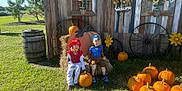 Christian joined the competition — help win amazing prizes! child, children, pumpkins, pumpkin_patch, hay_bale, costumes, outdoors, grass, wooden_wall, sunflower, wagon_wheel, barrel, autumn, fall_decor, smiling, sitting, portrait, seasonal_display, welcome_sign, family_event