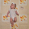 Genevieve is registered to the contest to win money with this photo: baby, blanket, bow, child, colorful, duck_pattern, floral_clothing, headband, indoor, infant, looking_up, lying_down, milestone_photo, onesie, portrait, quilt, safe, smiling, textile, three_months