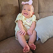 Genevieve joined the competition — help win amazing prizes! baby, barefoot, child, couch, cushion, dress, face, feet, furniture, happy, headband, home, indoor, infant, pink_bow, portrait, sitting, smiling, sofa, yellow_clothing