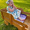 baby, child, outdoor, wagon, wooden_wagon, grass, sunlight, dress, bow, smile, happy, infant, greenery, summer, playful, cute, sitting, portrait, nature, childhood