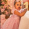 toddler, child, dress, pink, headband, bow, toy, flower_arrangement, fairy_lights, birthday, celebration, teddy_bear, curly_hair, portrait, indoor, soft_lighting, decor, cute, smiling, happy