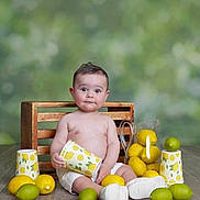 Karam is registered to the contest to win money with this photo: baby, child, lemon, lime, cup, pitcher, wooden_floor, crate, fruit, sitting, white_shoes, white_shorts, curious_expression, indoor, still_life, portrait, colorful, fresh, playful, smiling
