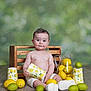 baby, child, lemon, lime, cup, pitcher, wooden_floor, crate, fruit, sitting, white_shoes, white_shorts, curious_expression, indoor, still_life, portrait, colorful, fresh, playful, smiling