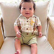 Ezaia is registered to the contest to win money with this photo: baby, child, smiling, sitting, indoors, chair, cushion, clothing, suspenders, shorts, hairstyle, window, natural_light, cute, portrait, feet, happy, person, infant, home