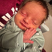 Oakley is registered to the contest to win money with this photo: newborn, baby, sleeping, hand, face, infant, clothing, green_outfit, snowman_print, cozy, cute, resting, peaceful, child, person, indoors, soft_light, closeup, portrait, tender_moment