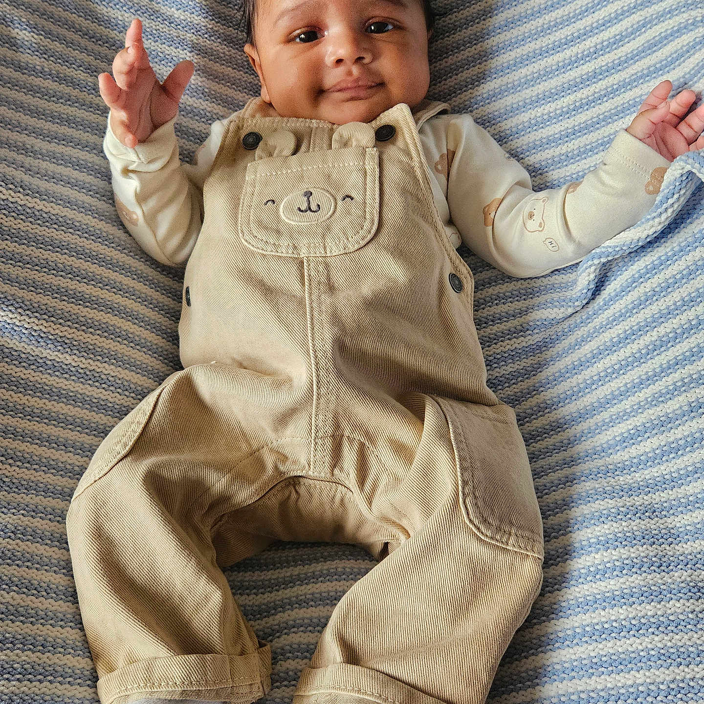 Kairi is registered to the contest to win money with this photo: adorable, baby, beige_clothing, casual, child, cozy, cute, face, happy, indoors, infant, lying_down, overalls, portrait, small_hands, smiling, soft_texture, striped_blanket, white_socks, young