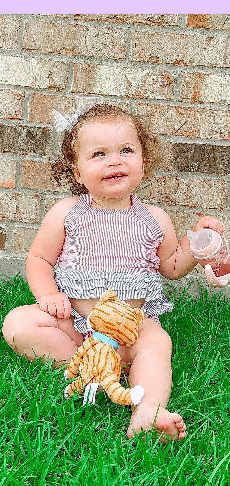 Princess Burleigh is registered to the contest to win money with this photo: baby, baby_toddler_clothing, child, dress, facial_expression, finger, fun, grass, green, happy, human_body, joy, pattern, people_in_nature, person, pink, plant, sitting, skin, smile