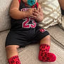 baby, infant, pacifier, socks, clothing, couch, pillow, hand, face, person, indoor, relaxing, cute, child, sporty, red, black, comfortable, apparel, portrait