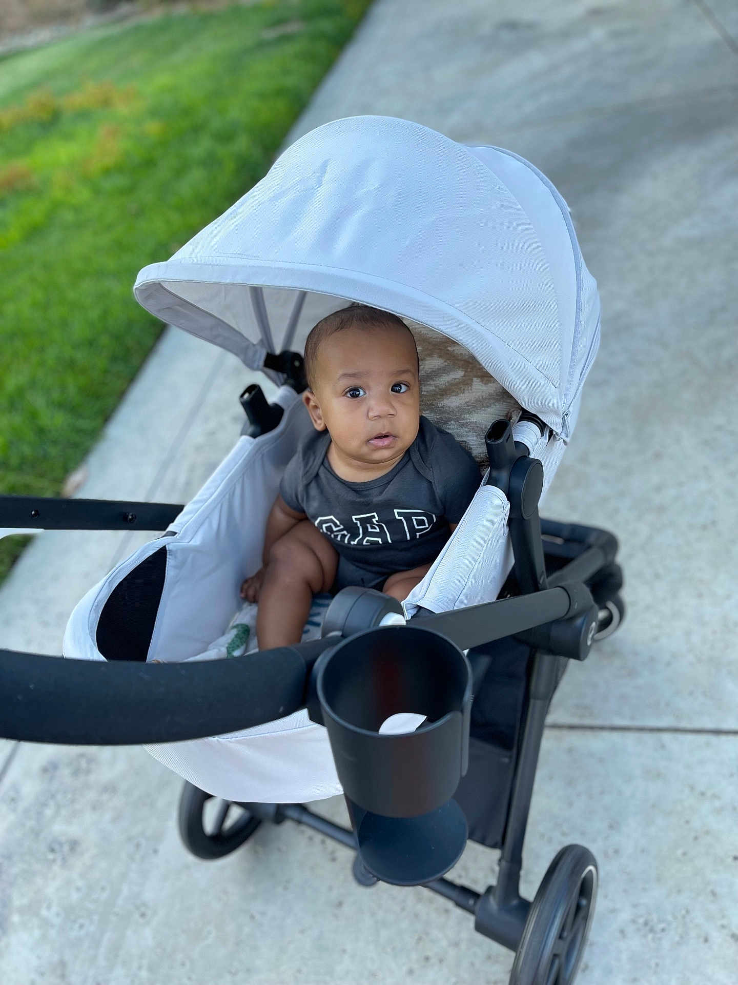 Raylan joined the competition — help win amazing prizes! baby, stroller, child, outdoor, sidewalk, grass, curious, infant, canopy, wheels, black_clothing, modern, seat, person, young_child, baby_girl_or_boy, daylight, pavement, casual, transportation