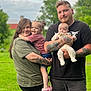 family, woman, man, toddler, baby, outdoor, greenery, grass, smile, holding, tattoos, casual_clothing, shorts, tshirt, happy, child, portrait, nature, daylight, people