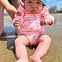 adult_support, baby, barefoot, beach, blue_hat, child, closeup, expression, hands, infant, legs, outdoor, palm_tree_pattern, pink_onesie, portrait, sand, serious_face, summer, sunny, water