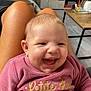 baby, child, clothing, couch, face, flooring, furniture, hand, happy, head, indoor, joy, living_room, person, pink_sweater, sitting, smiling, table, television, wooden_table