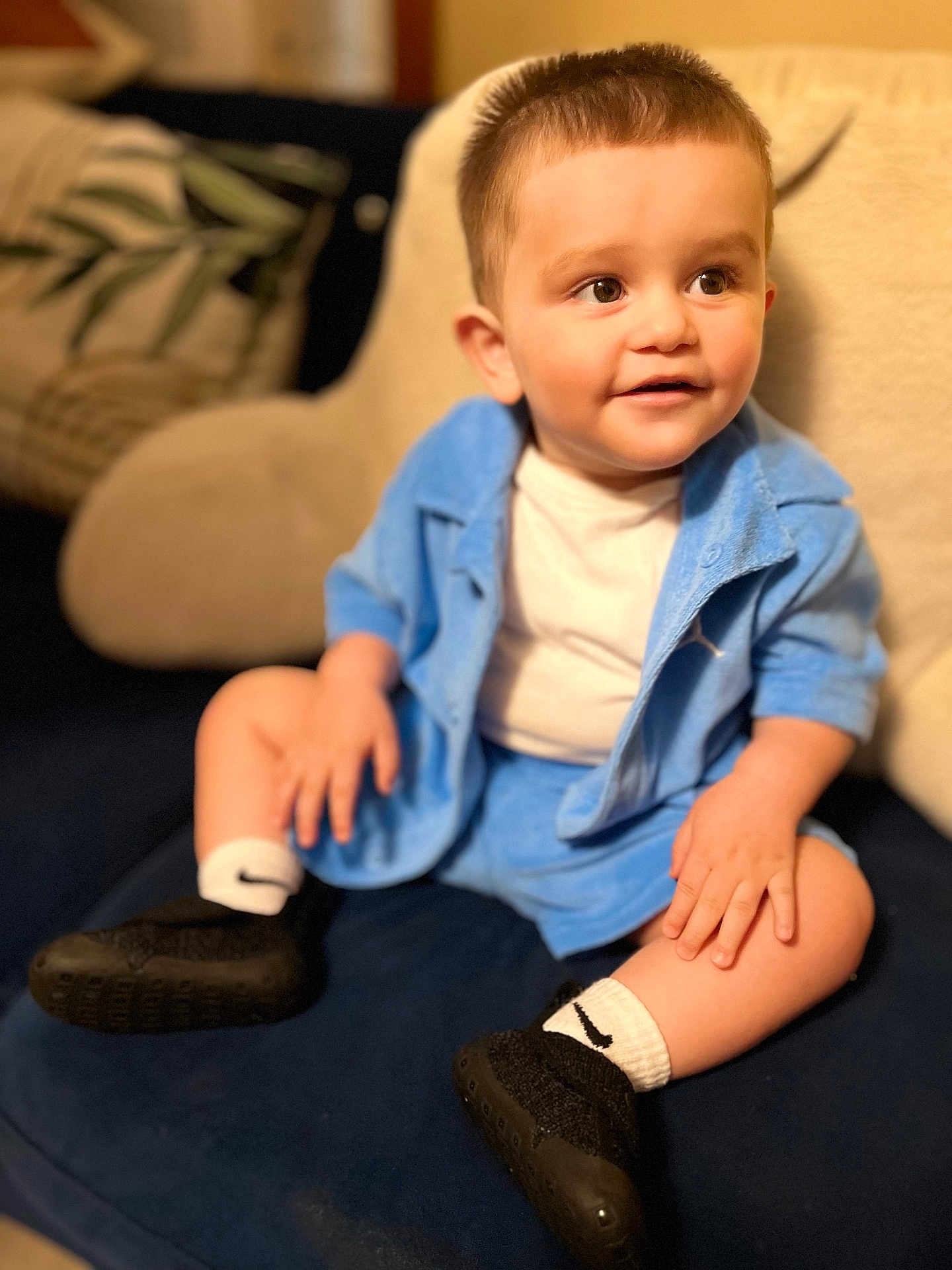 Jeishiel is registered to the contest to win money with this photo: toddler, child, blue_outfit, white_shirt, black_shoes, white_socks, couch, indoor, smiling, curious, seated, short_hair, hands, face, happy, cozy, soft_lighting, portrait, home, furniture