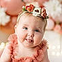 baby, child, face, blue_eyes, flower_crown, headband, dress, smiling, tongue_out, portrait, close_up, cute, infant, pink, peach, balloons, bokeh, soft_light, celebration, happy