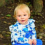 toddler, child, blonde_hair, blue_clothing, floral_pattern, outdoor, forest_floor, tree_trunk, leaves, sitting, cute, portrait, young_child, nature, rosy_cheeks, long_sleeves, pants, casual, innocent, curious