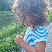 Sirine a rejoint le concours — aidez-le/la à gagner de superbes lots ! child, curly_hair, glasses, striped_shirt, dandelion, nature, river, grass, path, outdoor, daylight, blue_shorts, greenery, profile_view, casual_clothing, young_kid, summer, peaceful, exploration, curiosity