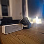 Timothy is registered to the contest to win money with this photo: anker, black_cat, blurred_background, cat, cozy, domestic_animal, electronics, feline, home, indoor, pet, quiet, relaxation, resting, soft_lighting, speaker, table_surface, technology, white_markings, wooden_table