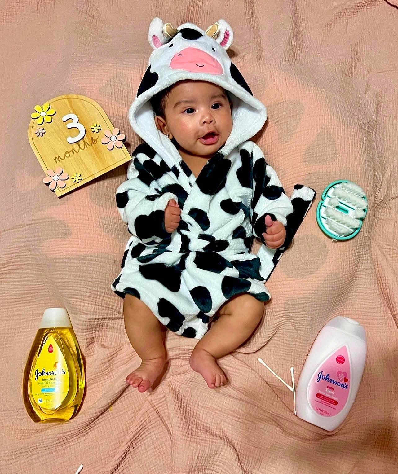 Zaylie is registered to the contest to win money with this photo: baby, infant, cow_print, robe, hood, ears, pink_blanket, wooden_sign, 3_months, baby_care, bottle, cotton_swabs, baby_lotion, baby_shampoo, cute, smiling, sitting, indoors, soft_texture, child