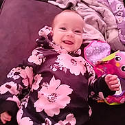 Hope-Rose joined the competition — help win amazing prizes! baby, smiling, floral_clothing, hoodie, plush_toy, blanket, couch, indoor, child, happy, face, person, infant, cute, soft_toy, portrait, lying_down, cozy, colorful, playful