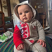 Sylas joined the competition — help win amazing prizes! baby, infant, hoodie, hood, face, eyes, hand, fingers, sitting, crocheted_blanket, wipes_package, zipper, casual_clothing, indoor, wood_paneling, door, chair, table, portrait, curious_expression