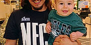 Kemp is registered to the contest to win money with this photo: man, baby, smile, indoor, store, clothing, green_shirt, socks, holding, happy, person, face, long_hair, beard, goatee, sign, lighting, background, retail, family