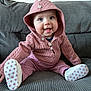 baby, baby_shoes, buttoned_hoodie, child, clothing, couch, cute, face, footwear, gray_couch, happy, heart_pattern, hood, indoor, infant, pink_hoodie, portrait, seated, small_child, smiling