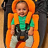 baby, child, smiling, orange_cushion, green_shirt, striped_pants, baby_seat, wooden_floor, black_fabric, happy, infant, sitting, indoor, cute, portrait, childcare, baby_toy, star_shaped_toy, comfort, face