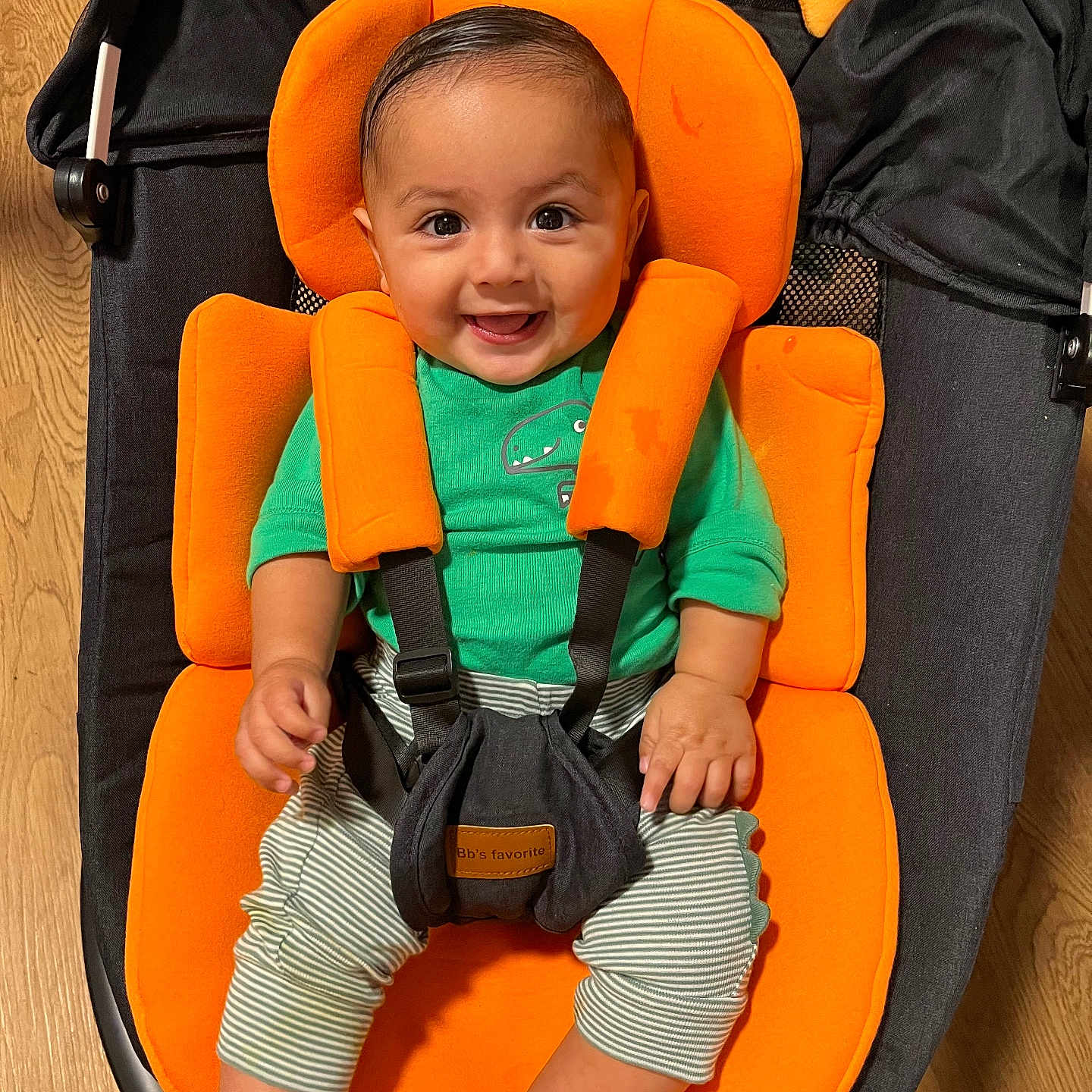 Zayden joined the competition — help win amazing prizes! baby, child, smiling, orange_cushion, green_shirt, striped_pants, baby_seat, wooden_floor, black_fabric, happy, infant, sitting, indoor, cute, portrait, childcare, baby_toy, star_shaped_toy, comfort, face