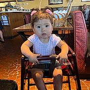 Sophia Grace is registered to the contest to win money with this photo: basket, brown_hair, casual_clothing, child, curious_expression, floor_tiles, high_chair, indoor, light_fixture, people_in_background, person, pink_hair_clips, pink_shoes, restaurant, safety_strap, seat, table, toddler, wall_art, wooden_table