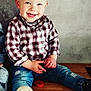 casual_clothing, child, cute, face, fashion, footwear, happy, indoor, jeans, person, plaid_shirt, playful, portrait, short_hair, sitting, smiling, toddler, toy, wall_art, wooden_floor
