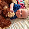 Joshua is registered to the contest to win money with this photo: baby, teddy_bear, stuffed_animal, blue_shirt, bed, blanket, smile, happy, cuddling, infant, child, soft_toy, plush, lying_down, indoor, comfort, cute, person, face, skin