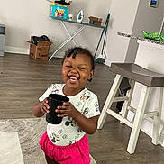 Leani is registered to the contest to win money with this photo: toddler, child, smiling, indoor, floor, socks, cup, hair_beads, shorts, tshirt, minnie_mouse, carpet, ironing_board, box, stool, broom, kitchen_counter, wood_floor, happy, standing