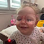 toddler, child, glasses, remote_control, pajamas, polka_dots, smile, indoor, living_room, toy, couch, cushion, happy, person, baby, face, furniture, window, curtain, home