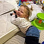 toddler, child, smile, remote_control, mattress, carpet, toy, indoor, clothing, jeans, long_sleeve_shirt, playtime, furniture, hair_tied, face, person, happy, cushion, green_stool, room