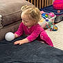 toddler, child, pink_clothing, toy_ball, black_blanket, sofa, baby_gate, toys, storage_bin, carpet, indoor, curly_hair, playtime, colorful_toys, floor, candid, exploration, home, young_child, baby