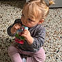 toddler, child, juice_pouch, sitting, blonde_hair, pigtails, grey_top, pink_pants, socks, floor, indoor, drinking, cute, young_child, baby_food, expression, person, casual_clothing, portrait, concentration