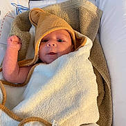 Kaïs a rejoint le concours — aidez-le/la à gagner de superbes lots ! baby, towel, hooded_towel, infant, wrapped, lying_down, soft_texture, cushion, blanket, indoors, curious_expression, face, skin, newborn, comfort, warm_lighting, closeup, person, child, resting