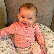 Aunaleigh is registered to the contest to win money with this photo: baby, child, smiling, pink_clothing, knitted_pants, socks, couch, pillow, koala_pattern, floral_pattern, happy, indoors, cute, person, seated, infant, cozy, home, soft_fabric, portrait