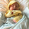 Jameson is registered to the contest to win money with this photo: baby, sleeping, yellow_clothing, hat, blanket, bed, cute, infant, peaceful, soft_lighting, indoors, cozy, child, portrait, newborn, resting, wrapped, smiling_face, warm, comfortable