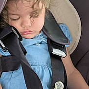 Inaya participe au concours pour gagner de l'argent avec cette photo : toddler, sleeping, car_seat, curly_hair, baby_bottle, blue_dress, child, seatbelt, infant, travel, peaceful, young_child, safety, nap, indoor, person, cute, hands, clothing, resting