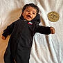 baby, infant, black_onesie, nike_logo, curly_hair, smiling, white_blanket, wooden_sign, two_months, lying_down, cute, happy, portrait, child, indoor, soft_texture, milestone, small_hand, cozy, expression
