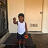 Darius Warren is registered to the contest to win money with this photo: black_shorts, black_sneakers, casual_clothing, child, concrete_floor, door, doormat, expression, flower, front_view, headwrap, outdoor, person, pointing, porch, single_person, standing, toddler, white_tank_top, young_child