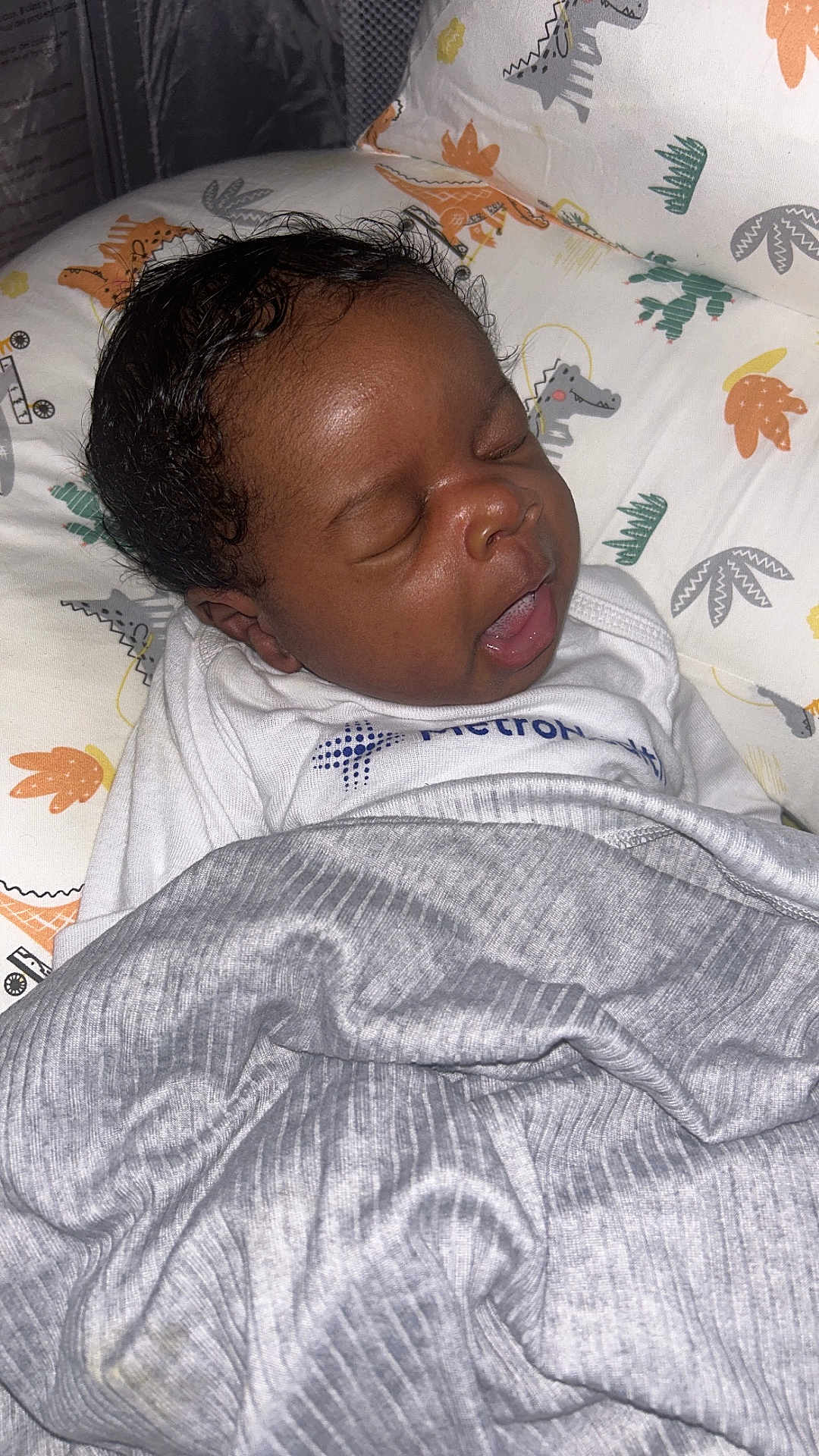 André joined the competition — help win amazing prizes! baby, sleeping, blanket, pillow, dinosaur_pattern, infant, cozy, mouth_open, curly_hair, soft_lighting, indoors, cute, resting, child, white_clothing, fabric, portrait, peaceful, young, face