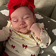 Kiara is registered to the contest to win money with this photo: baby, bows, child, clothing, cloud_pattern, cozy, cushion, cute, hand_on_cheek, headband, indoor, infant, peaceful, portrait, red_bow, resting, sleeping, smiling, soft_lighting, sweater