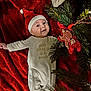 baby, infant, santa_hat, christmas, holiday, red_blanket, pine_branches, gingerbread_ornament, festive, smiling, cute, onesie, lying_down, face, headwear, celebration, decorations, holiday_season, cheerful, indoor