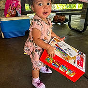 Selena is registered to the contest to win money with this photo: toddler, child, toy_box, curly_hair, minnie_mouse, pink_outfit, socks, cooler, bag, princess, outdoor, pavilion, concrete_floor, daylight, earrings, expression, holding, play, cute, standing