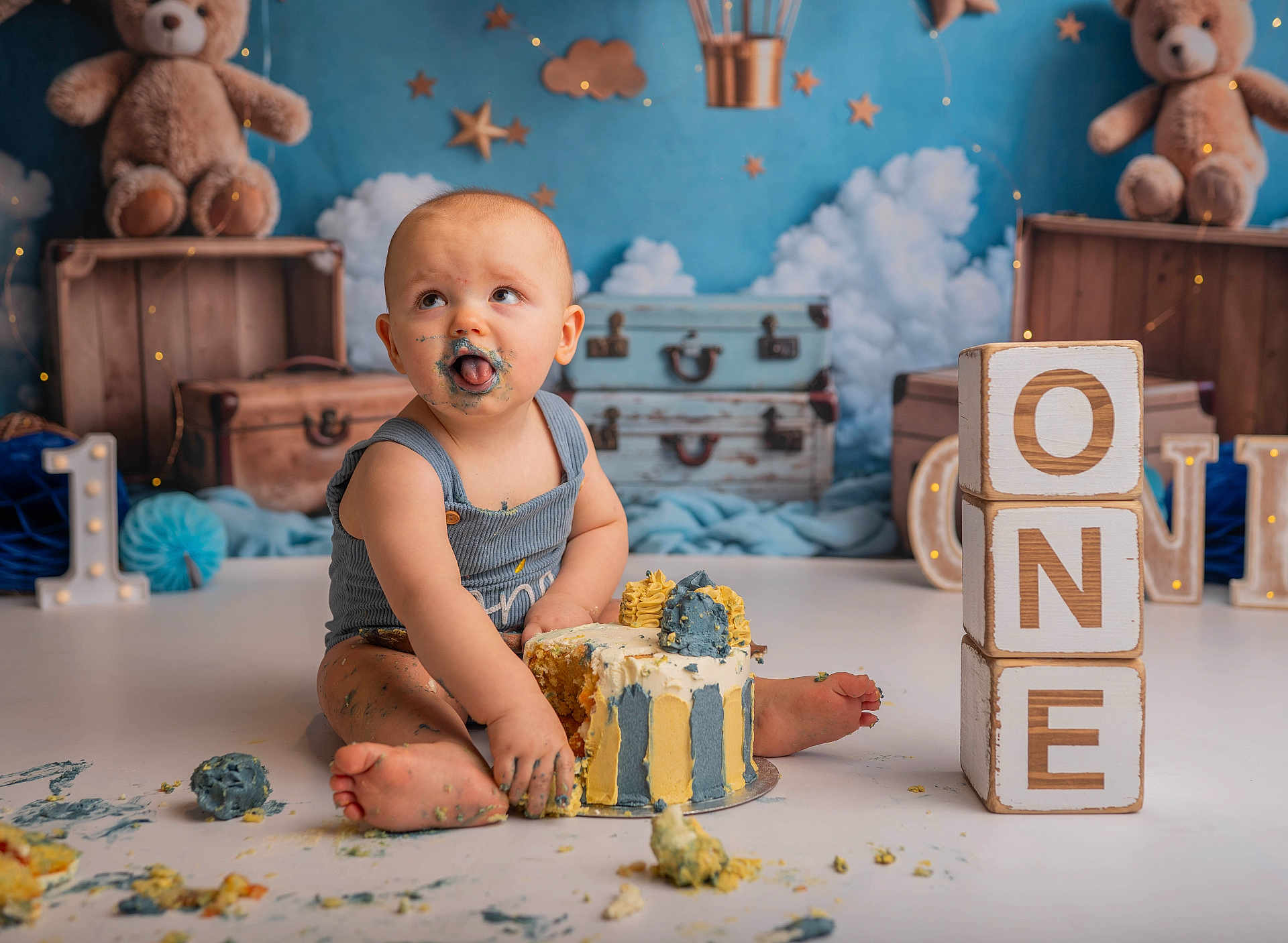 Karter Lee is registered to the contest to win money with this photo: baby, cake, birthday, messy, blue, yellow, frosting, blocks, one, teddy_bear, toy, background, clouds, stars, suit, floor, child, smudged, celebration, cute