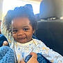Anthony is registered to the contest to win money with this photo: toddler, child, baby, face, smile, hand, clothing, onesie, animal_print, curly_hair, car, seat, blanket, blue, cozy, portrait, indoor, natural_light, happy, cute